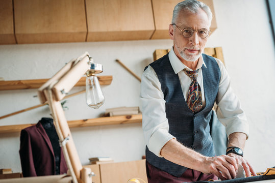 Handsome Mature Tailor Marking Cloth Pattern With Chalk At Sewing Workshop