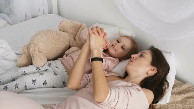 Mother and her little girl playing in the bed