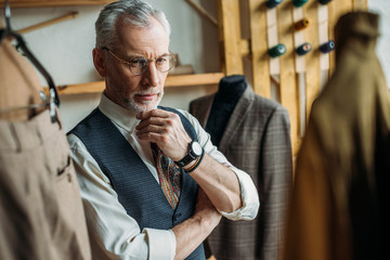 handsome mature man looking at jackets on hangers in store