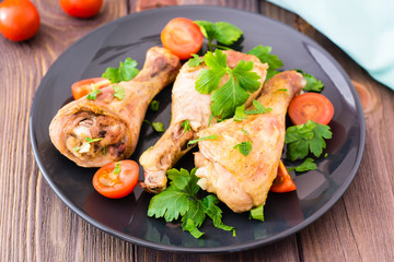 Baked chicken legs in spices with tomatoes and greens in a plate on a wooden table