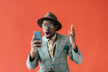 shocked african american man using smartphone, isolated on red