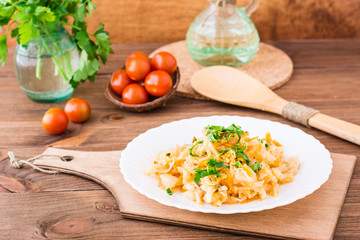 Stewed cabbage with tomato paste and fresh herbs in a plate, ripe cherry tomatoes and parsley on a wooden table