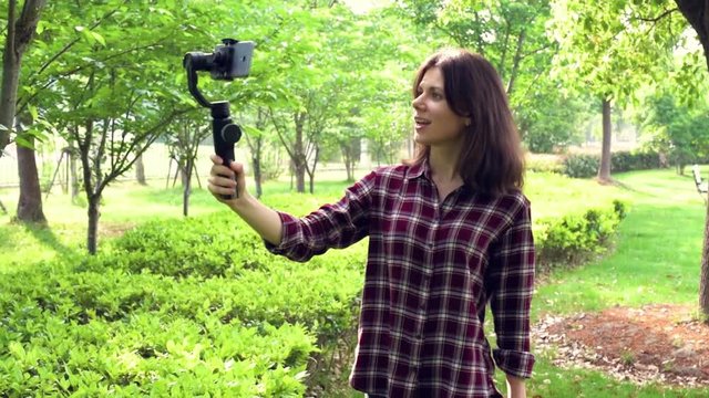Vlogger with mobile phone camera stabilizer recording outdoor video blog. A young pretty girl uses smartphone handheld gimbal for travel vlogging