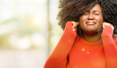 Beautiful african woman covering ears ignoring annoying loud noise, plugs ears to avoid hearing...