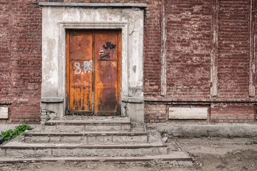 Old rusty closed door in aged brick wall. Abandoned building construction.