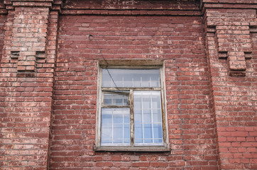 The old window with a lattice on aged brick wall of abandoned factory building.