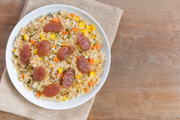 top view of fried rice with chinese pork sausage and vegetable in a ceramic dish on wooden table. homemade style food concept.