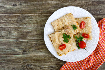 Pie, casserole pita with mushrooms, cottage cheese and cheese on a white plate on a wooden background. Layer Cake. The top view