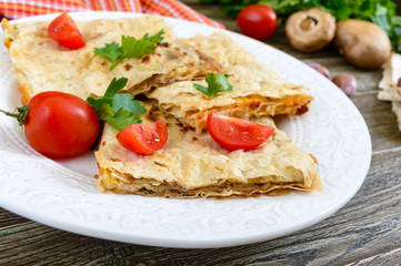 Pie, casserole pita with mushrooms, cottage cheese and cheese on a white plate on a wooden background. Layer Cake.