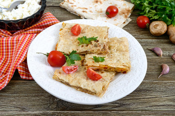 Pie, casserole pita with mushrooms, cottage cheese and cheese on a white plate on a wooden background. Layer Cake.
