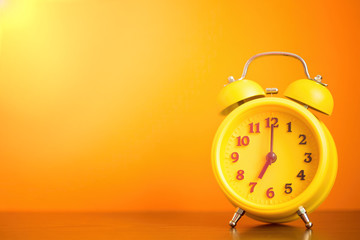 yellow alarm clock seven o'clock in the morning on the table against the orange wall. time for people to get to work, for kids to school, wake up