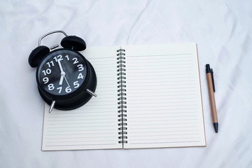 Diary or notebook and vintage alarm clock on bed in bedroom at home or hotel..