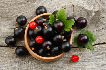 black currant in wooden bowl with green leaf on old wooden background. top view