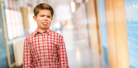Handsome toddler child with green eyes feeling disgusted with tongue out at school corridor © Krakenimages.com