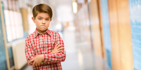 Handsome toddler child with green eyes nervous and scared biting lips looking camera with impatient expression, pensive at school corridor