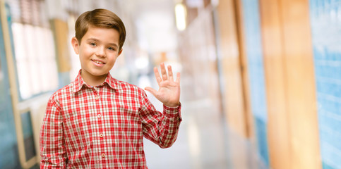 Handsome toddler child with green eyes raising finger, is the number five at school corridor © Krakenimages.com