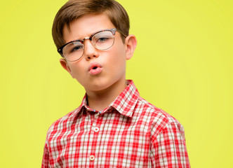 Handsome toddler child with green eyes happy and surprised cheering expressing wow gesture over yellow background