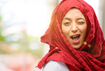 Young arab woman wearing hijab blinking eyes with happy gesture