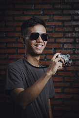 Asian Man Taking Picture With Vintage Camera Wearing Sun Glasses on Brick Wall Background