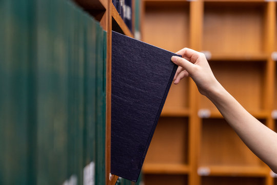 Hand pulling a Thesis book off the shelf in Library. Green colors books.