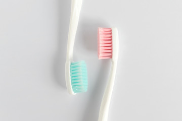 Close up of two plastic white toothbrushes with pink and blue bristle on white background. Free copy space.