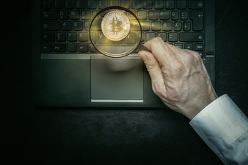 Mann untersucht mit Lupe eine physische Bitcoin Münze die leuchtet