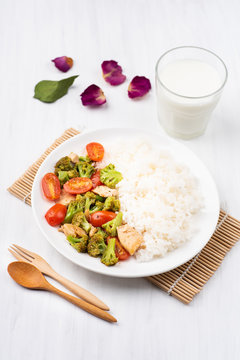 Fried broccoli with tomatoes, chicken and cooked rice on white dish and glass of milk, Asian cuisine