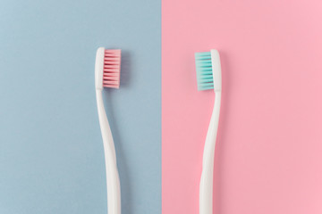 Close up of two plastic white toothbrushes with pink and blue bristle on pink and blue background. Free copy space.