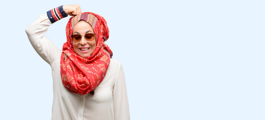 Middle age muslim arab woman wearing hijab doubt expression, confuse and wonder concept, uncertain future isolated blue background