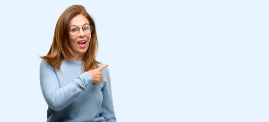 Middle age woman wearing wool sweater and cool glasses pointing away side with finger isolated blue background