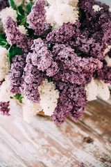 Bouquet of white and purple lilac flowers in wicker basket on ta
