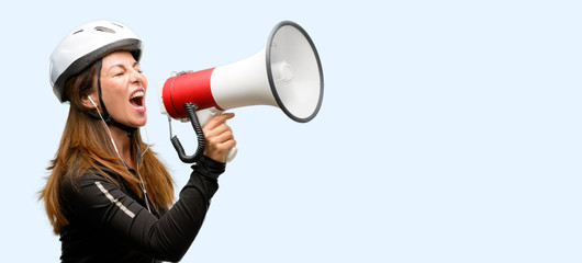 Middle age cyclist woman using earphones communicates shouting loud holding a megaphone, expressing...