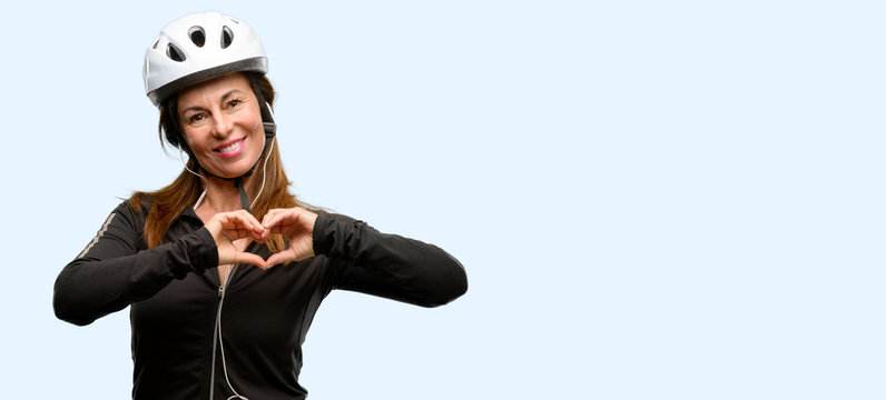 Middle age cyclist woman using earphones happy showing love with hands in heart shape expressing healthy and marriage symbol isolated blue background