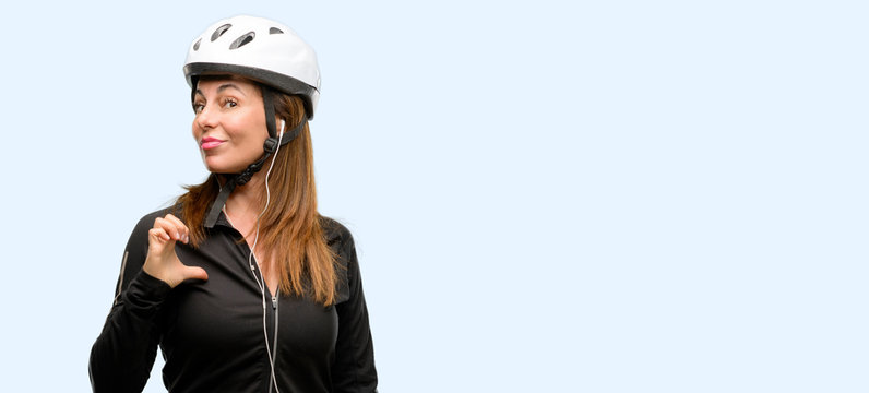 Middle age cyclist woman using earphones proud, excited and arrogant, pointing with victory face isolated blue background