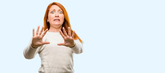 Beautiful young redhead woman disgusted and angry, keeping hands in stop gesture, as a defense,...