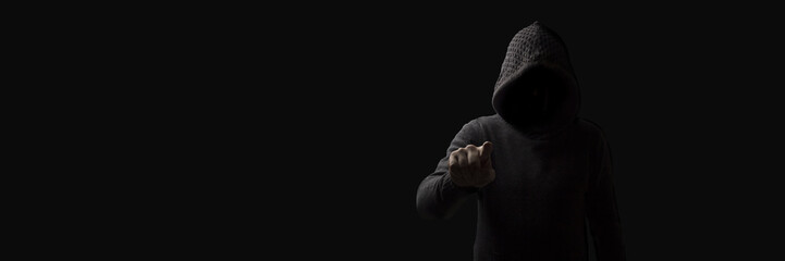 Faceless man in a hood with points a finger at the viewer on a dark background. Concept Threats and Terror