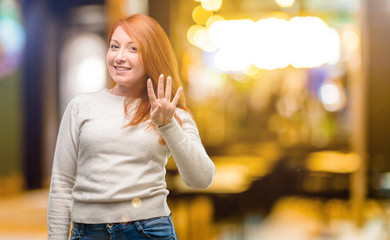 Fototapeta premium Beautiful young redhead woman raising finger, is the number four at night