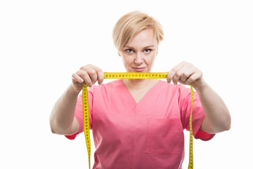 Attractive female nurse wearing pink scrubs holding measuring tape