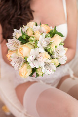 morning bride, the bride is holding a wedding bouquet and sits in a beautiful underwear in a white armchair