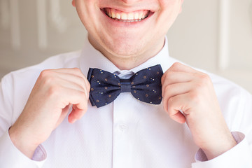 morning groom, the groom straightens the butterfly on his shirt and smiles