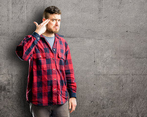 Young handsome man unhappy making suicide gesture, tired of everything. Shoots with his hand imitating gun, upset