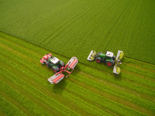 Aerial view of two tractor mowing a green fresh grass field, 
 farmer in a modern tractors mowing...