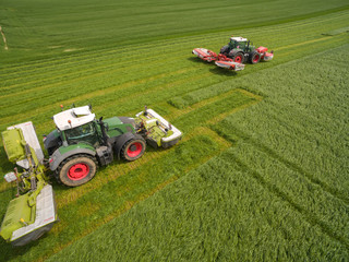 Aerial view of two tractor mowing a green fresh grass field, 
 farmer in a modern tractors mowing...