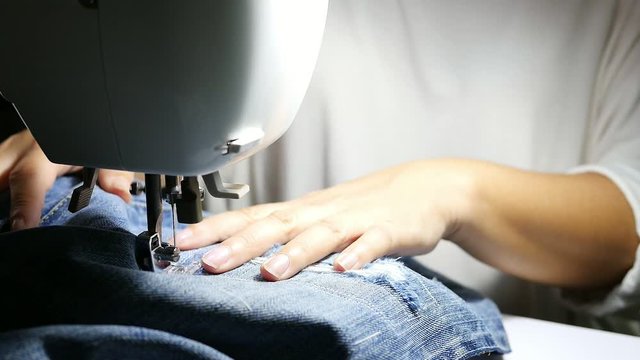 Woman doing jeans patchwork using sewing machine - home DIY sewing concept