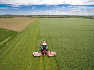 
Aerial view of a farmer in a modern tractor mowing a green fresh grass field on a sunny day with...