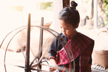 Cute asian child girl in Thai traditional dress using traditional wooden spinning wheel with fun...