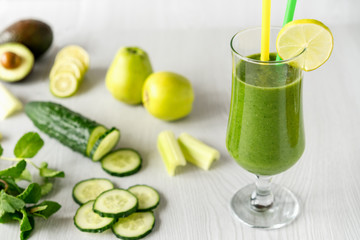 A glass of green vegetable smoothies on a white wooden background