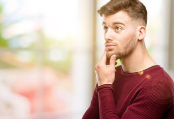 Handsome young man thinking and looking up expressing doubt and wonder