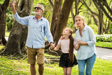 Happy family having fun together in the garden. Father, mother and daughter holding hands and walking in a park. Lifestyle concept