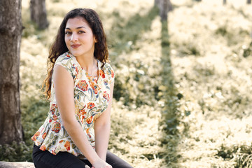 happy young girl sitting on a log in the forest, bright sunlight around, beauty of nature in spring